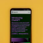 Mobile phone displaying the ChatGPT introduction screen with OpenAI branding on a yellow background.